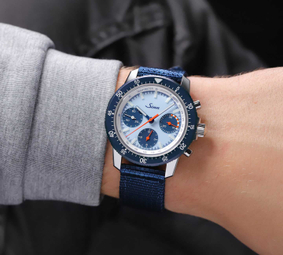 Die Sinn 103 St Sa Ty Hd H – getragen am Handgelenk, mit blauem Textilband, blauer Lünette und orangefarbenen Chronographenzeigern auf hellem Zifferblatt.