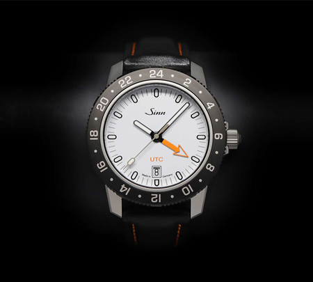 Sinn 105 St Sa UTC W avec cadran blanc, aiguille flèche UTC orange et bracelet en cuir noir.