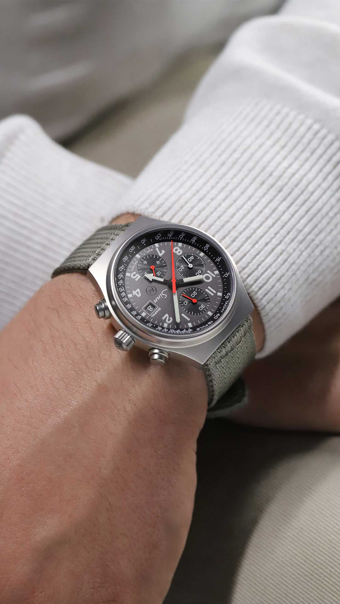Sinn 144 St DIAPAL with stainless-steel case, grey dial, red and white hands, and textile strap on the wrist.