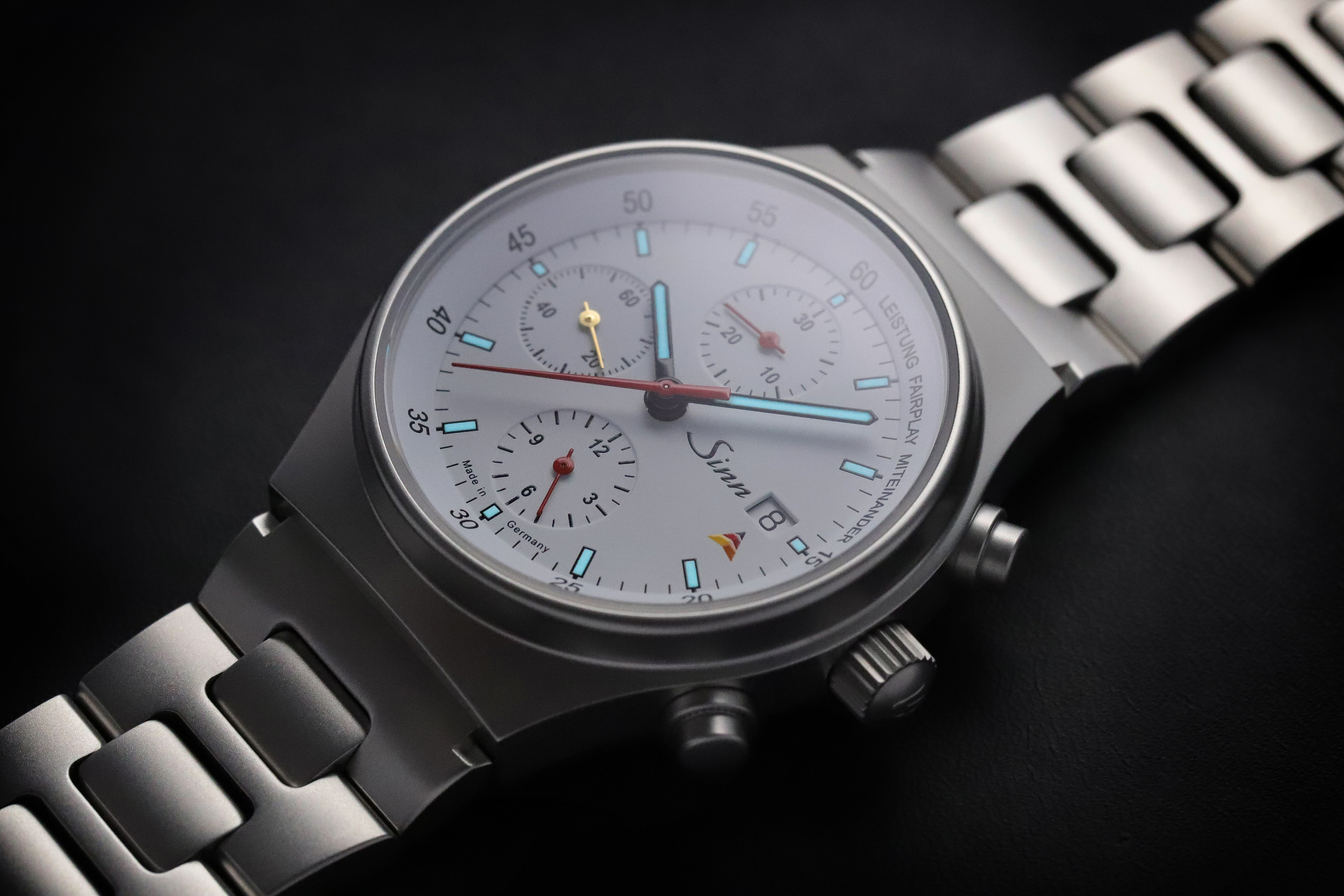 Close-up of a Sinn chronograph with white dial, three subdials, and luminous indices.