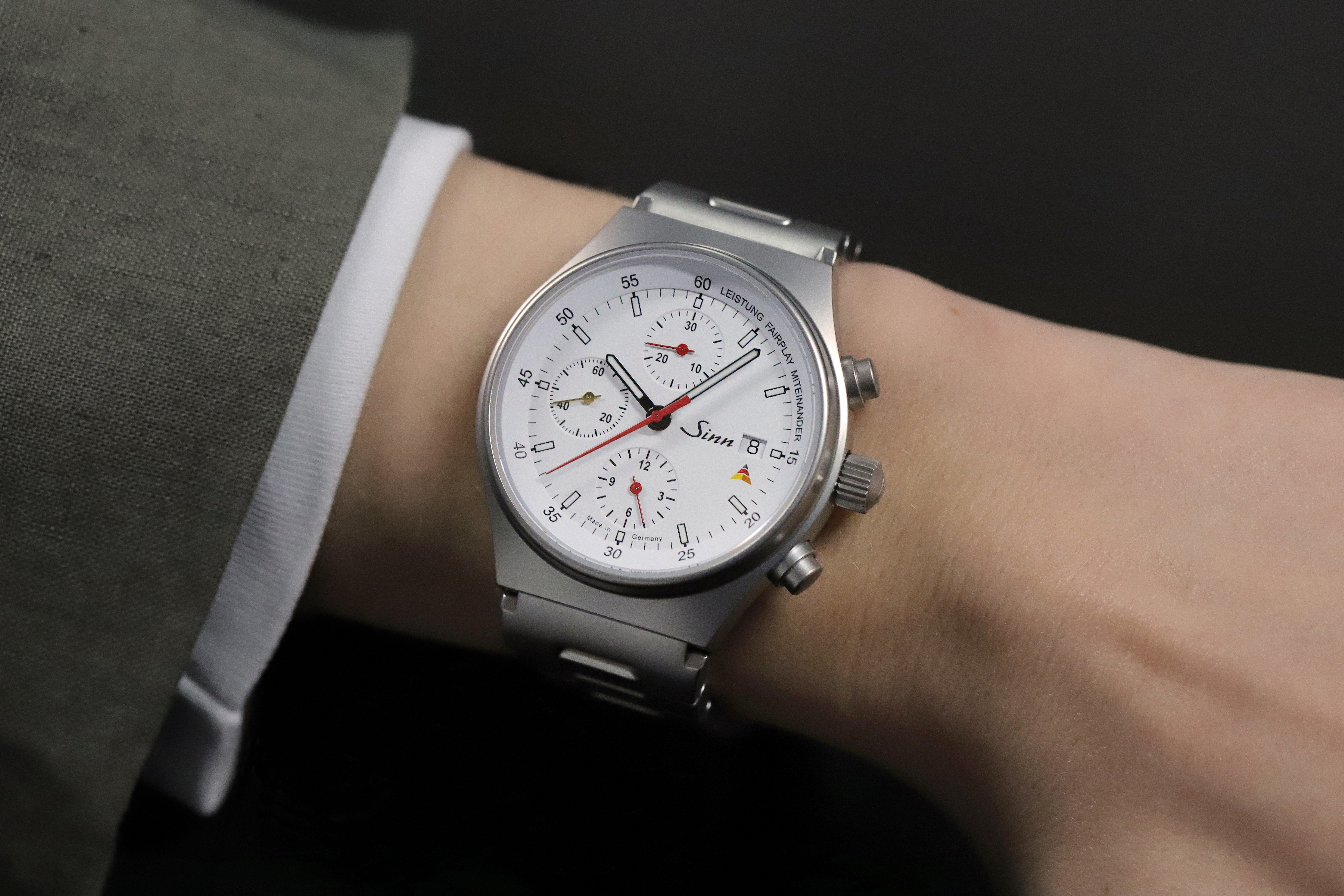 Sinn chronograph with white dial and solid stainless steel bracelet worn on a wrist.