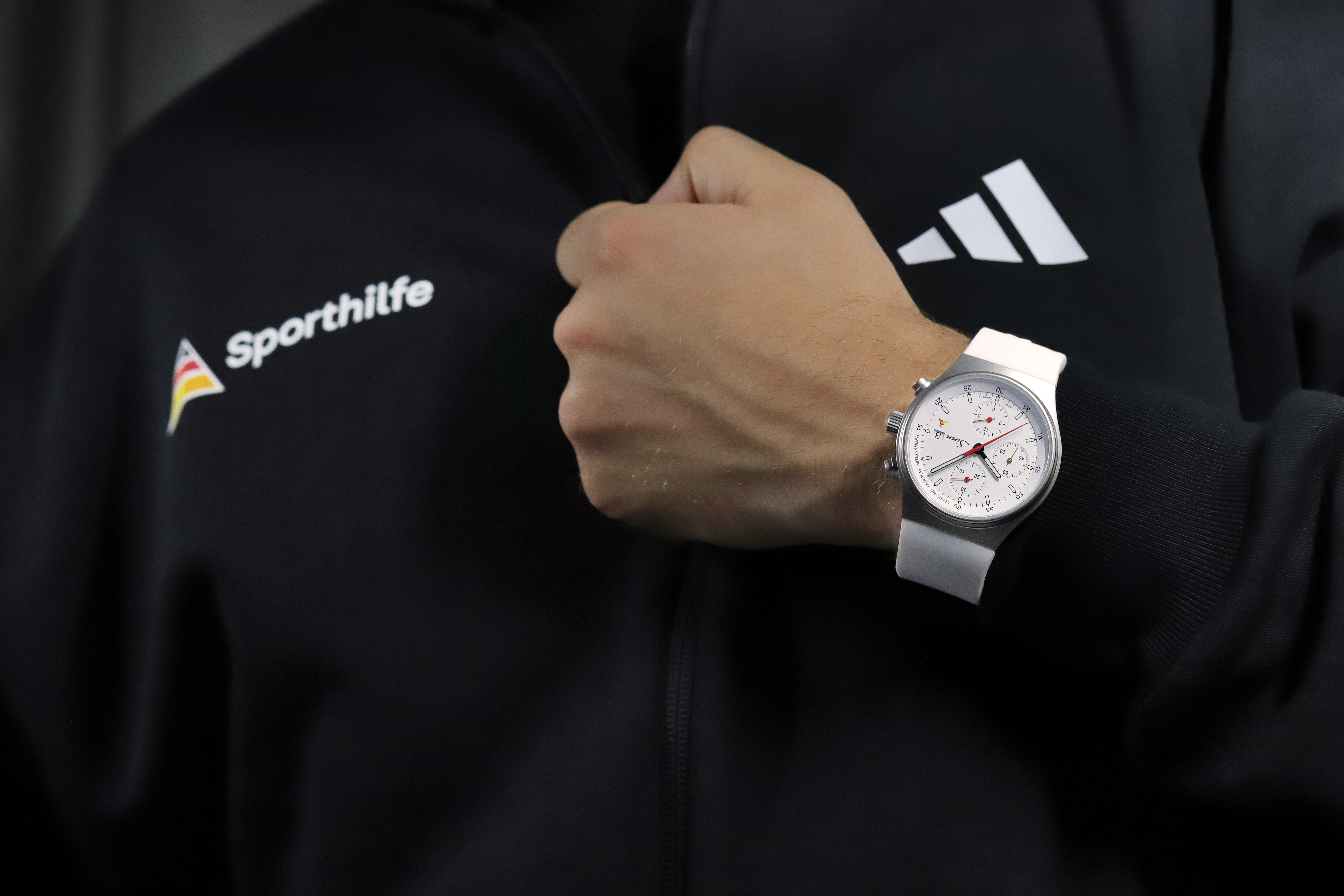 Sinn chronograph with white dial and white silicone strap worn on a wrist against a dark background.