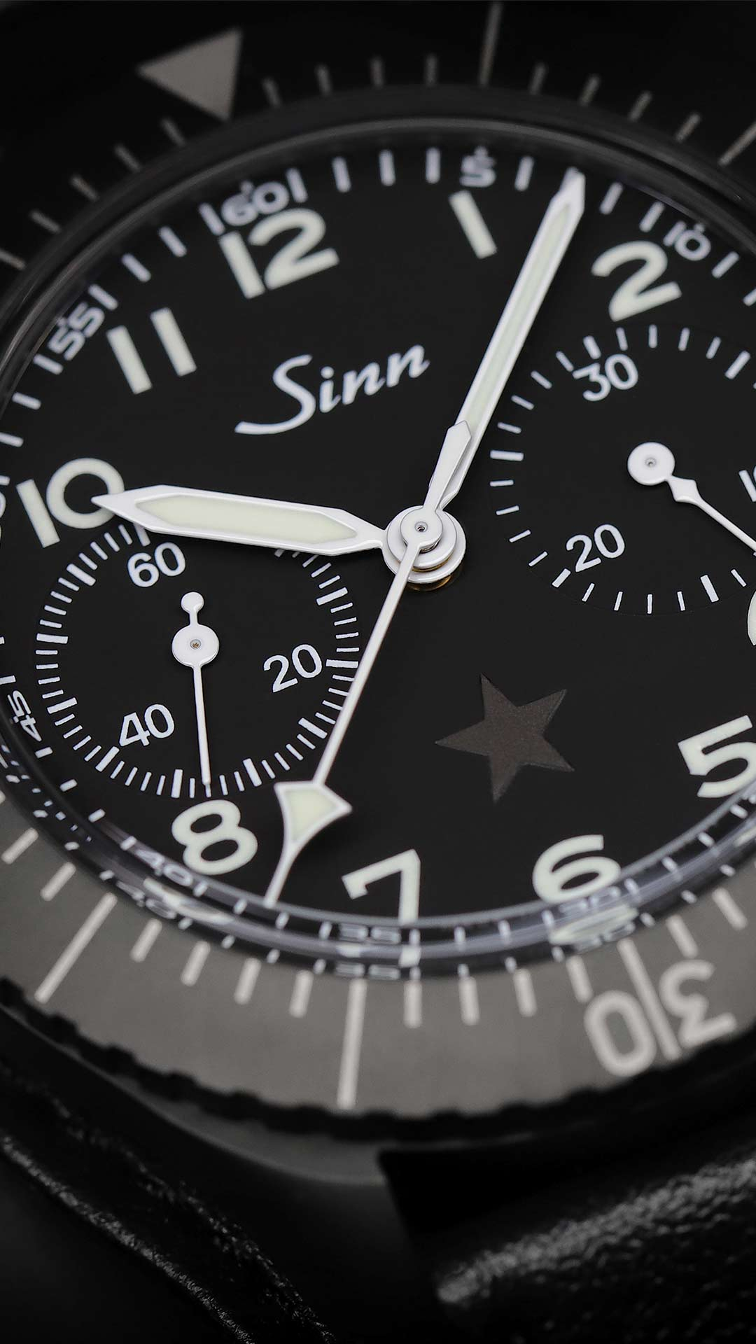 Sinn 155 S Revolution II with black case, black dial, white hands and leather strap, close-up of dial with star.