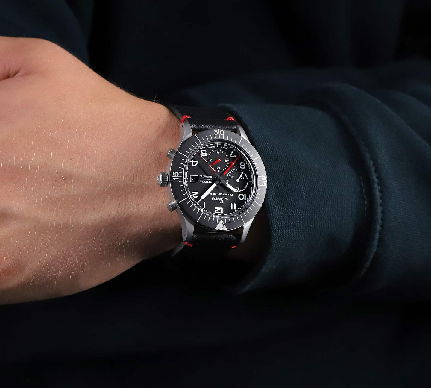 Sinn 156.1 am Handgelenk mit schwarzem Lederband und roten Nähten.