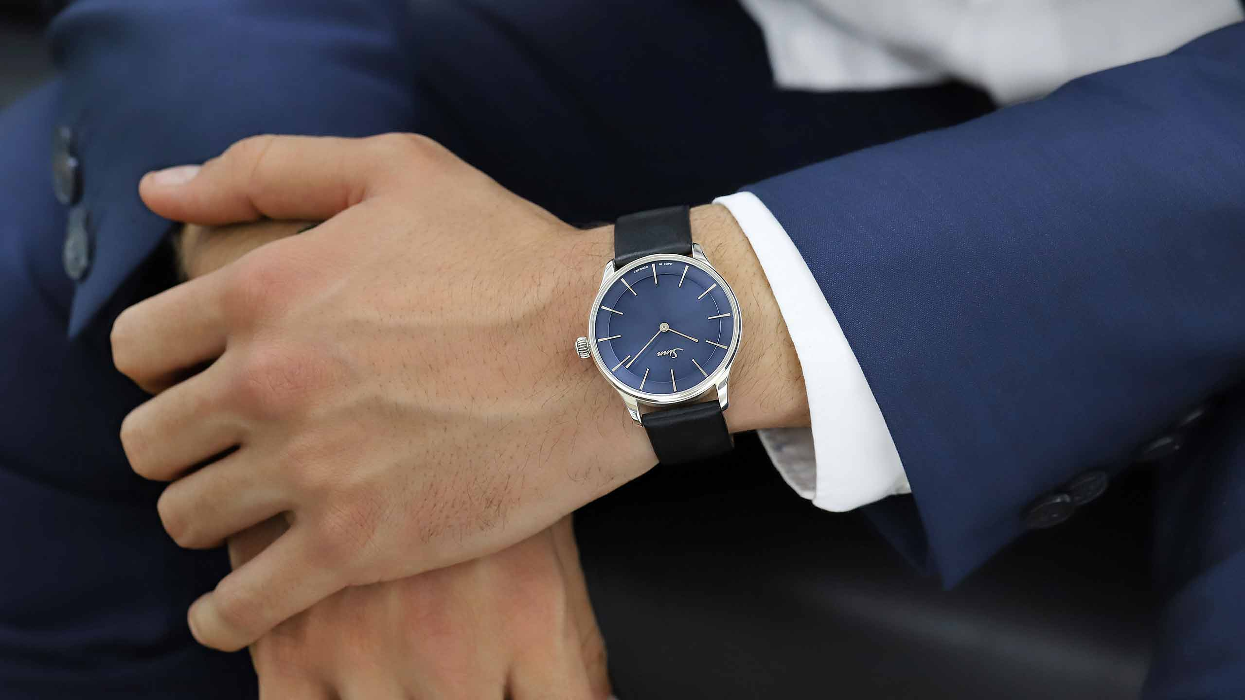                       Sinn 1739 Ag B with blue dial and black leather strap on the wrist in a suit.
                  