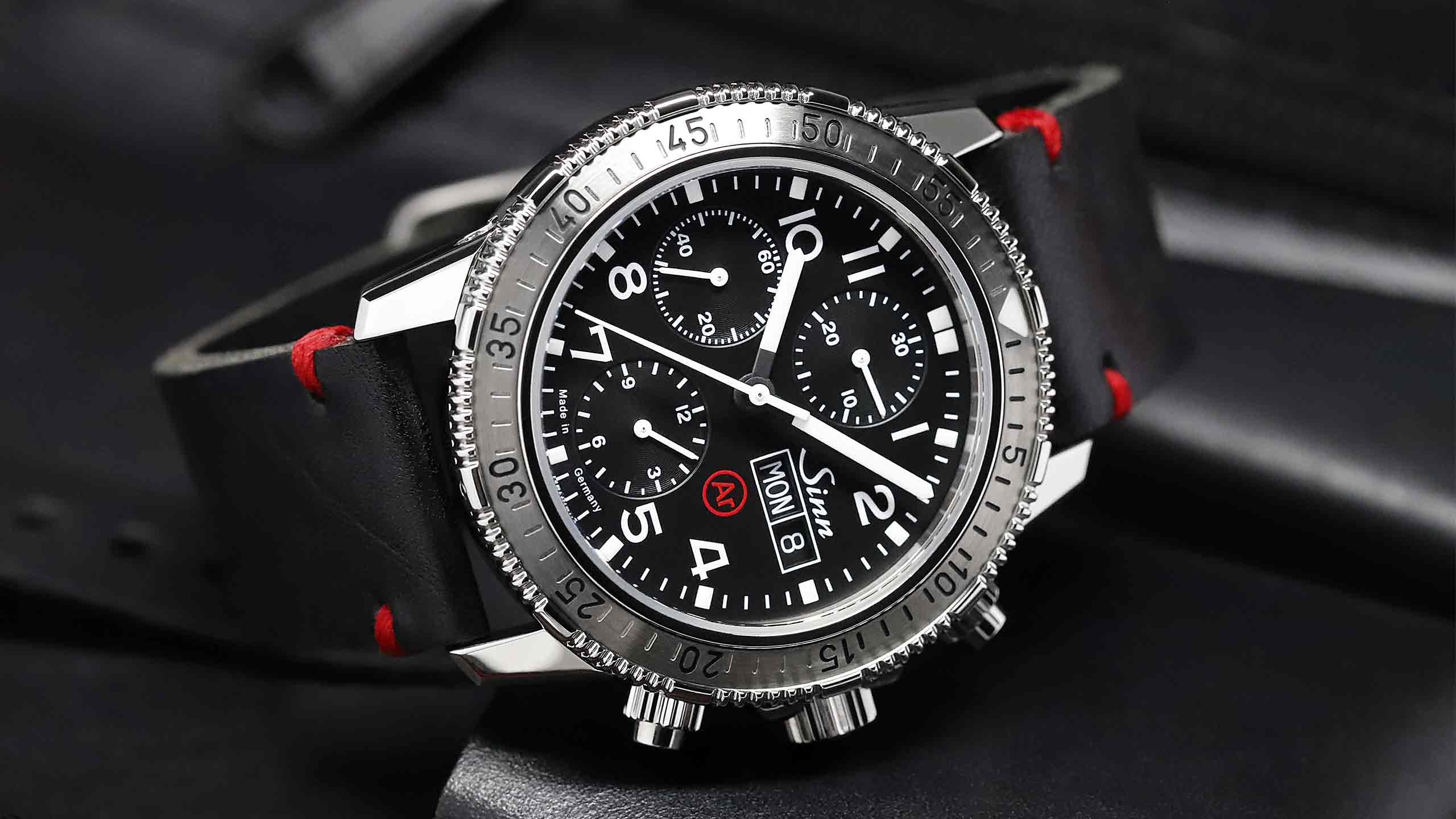                       Sinn 206 St Ar mit schwarzem Zifferblatt, Lederband mit roten Nähten und markanter Drehlünette.
                  