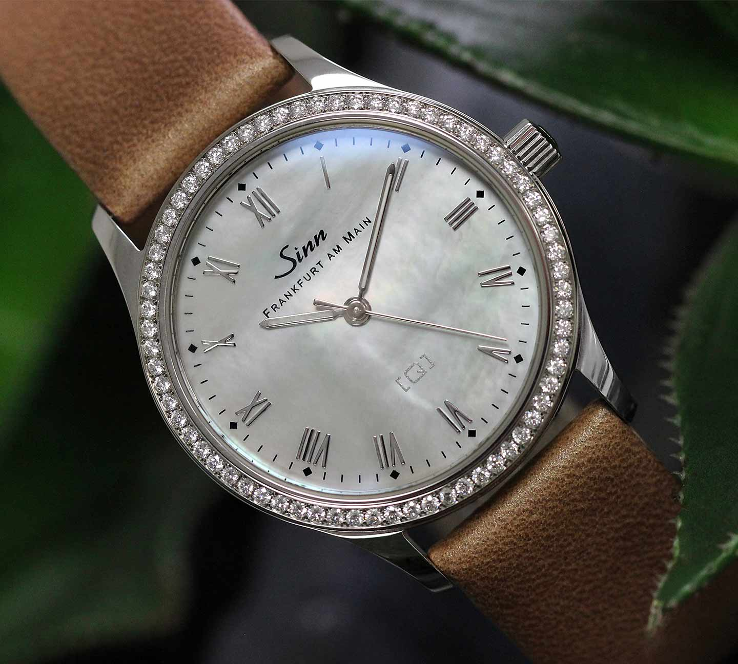 Elegante Damenuhr Sinn 434 TW68 WG Perlmutt W mit diamantbesetzter Weißgoldlünette und Perlmuttzifferblatt, präsentiert am braunen Lederband.