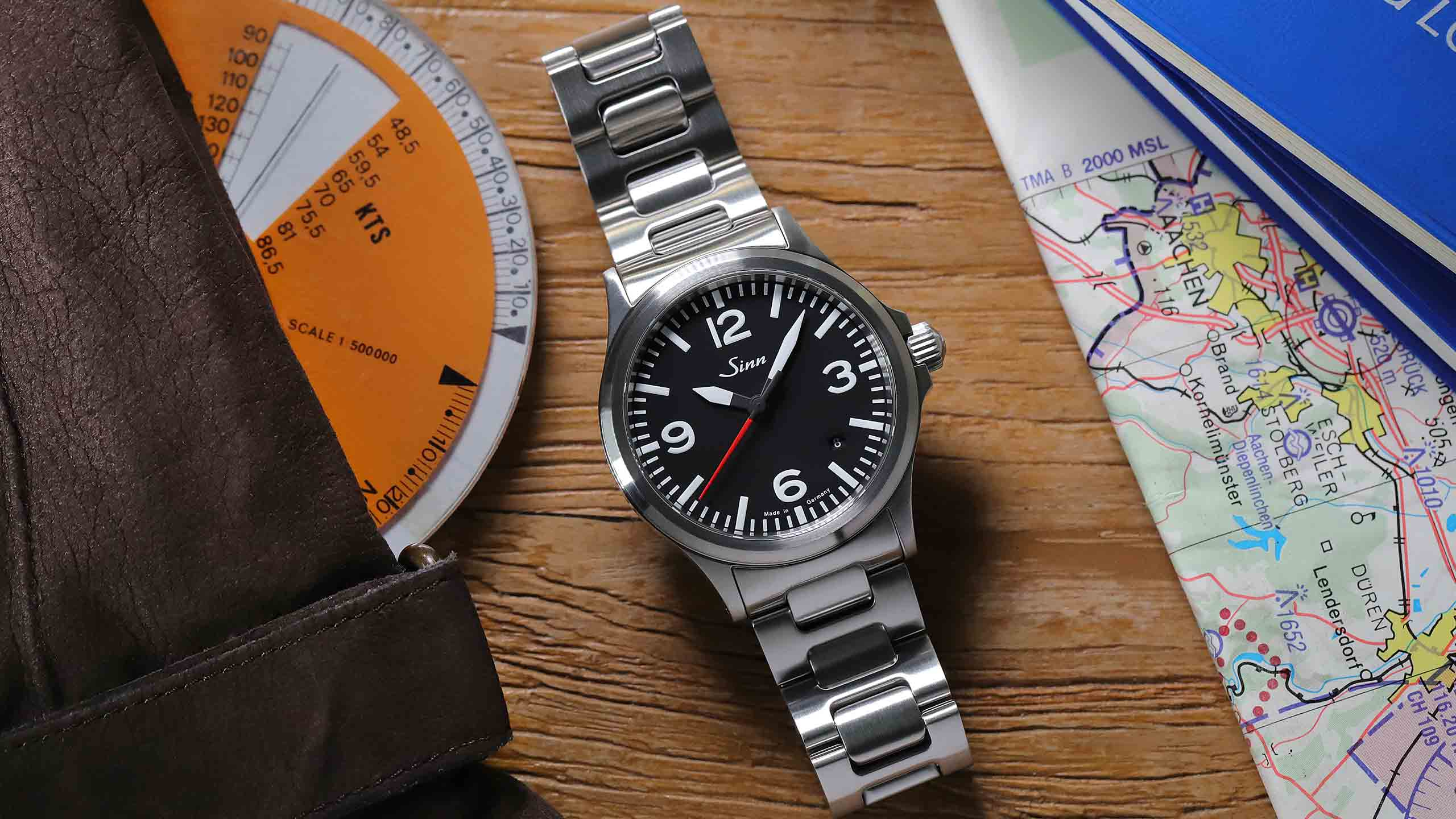                       Sinn 556 A RS avec bracelet en acier inoxydable, posée sur des cartes et accessoires de pilote.
                  