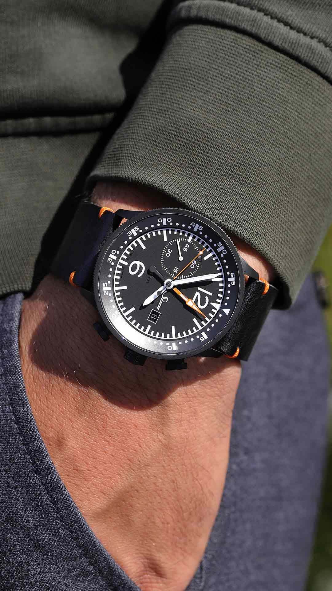Sinn 717 am Handgelenk mit schwarzem Lederband und orangefarbenen Nähten.