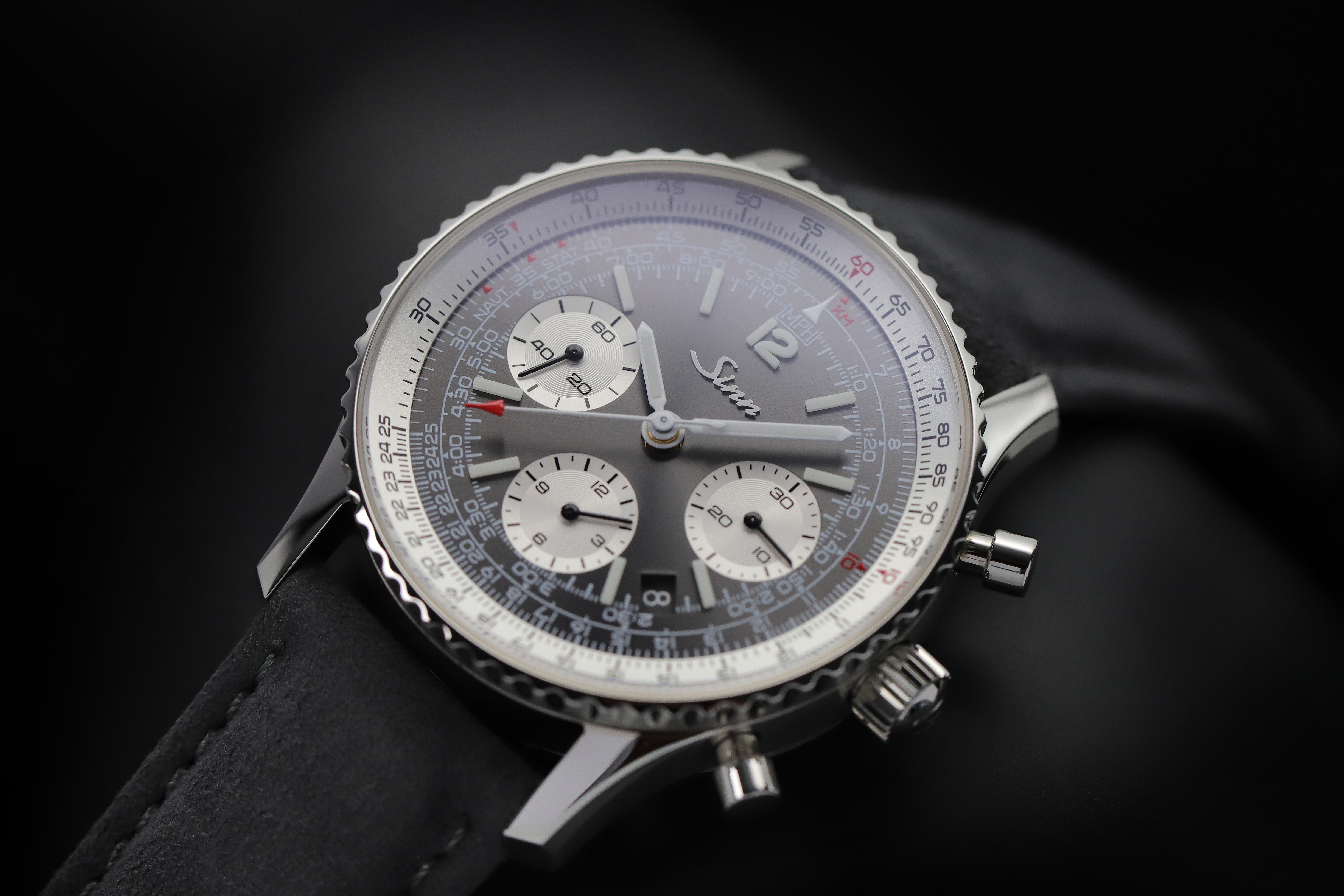                       Close-up of a Sinn chronograph with anthracite dial, three subdials, and slide rule bezel against a dark background.
                  