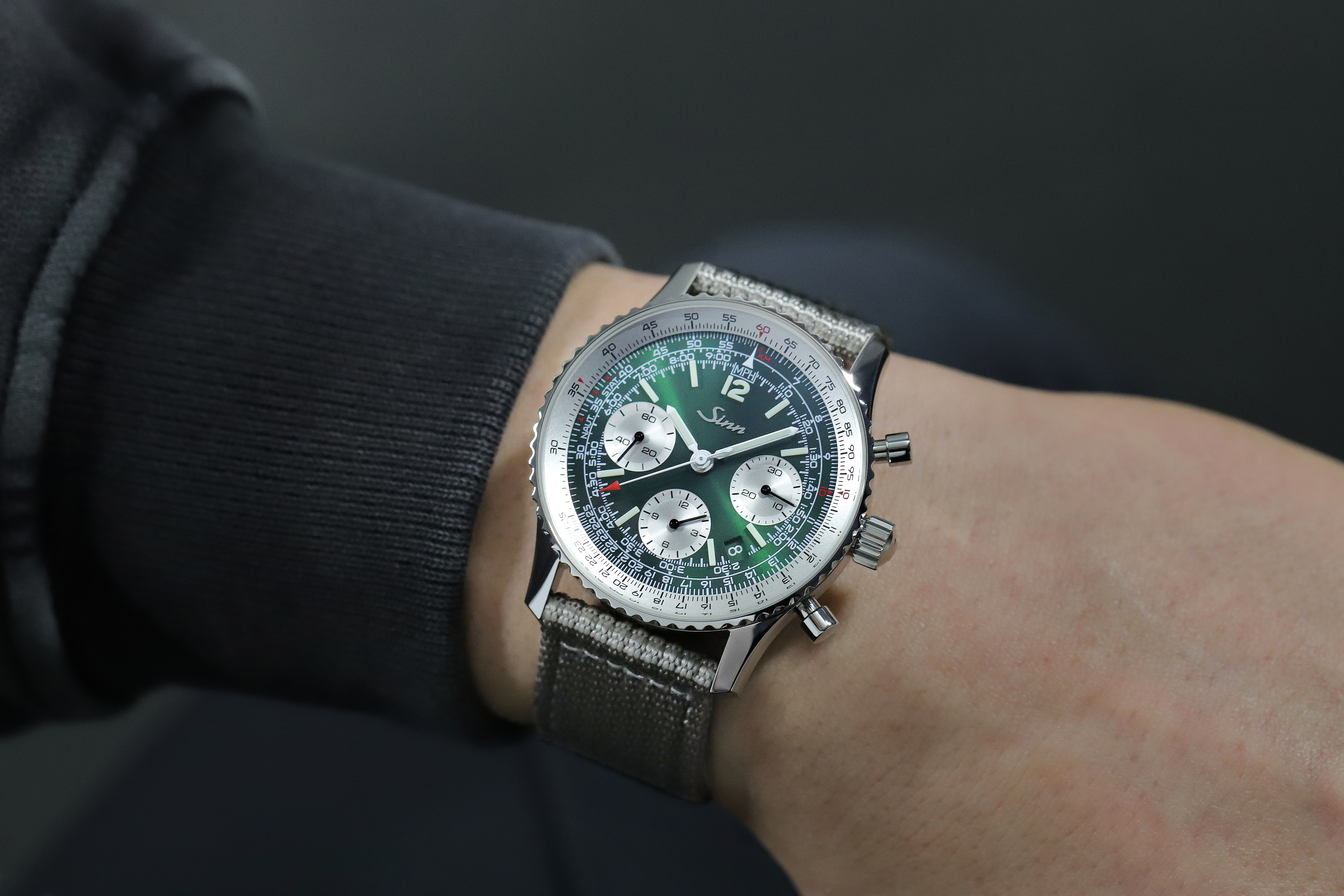                       Sinn chronograph with green dial, slide rule bezel, and grey textile strap worn on a wrist.
                  