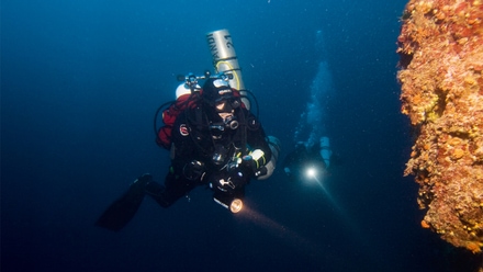 Wreck diver Andreas Peters on a dive in the North Sea with diving equipment and lamp, near a vegetated underwater structure.