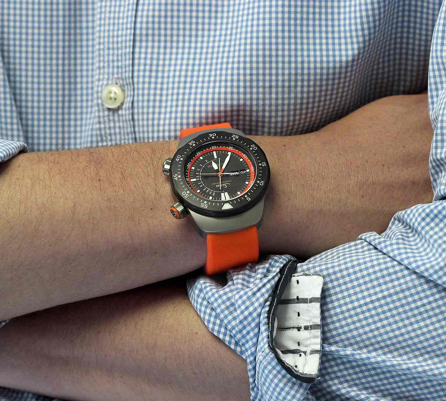 Sinn EZM 12 mit orangefarbenem Silikonband am Handgelenk, getragen zu einem karierten Hemd.