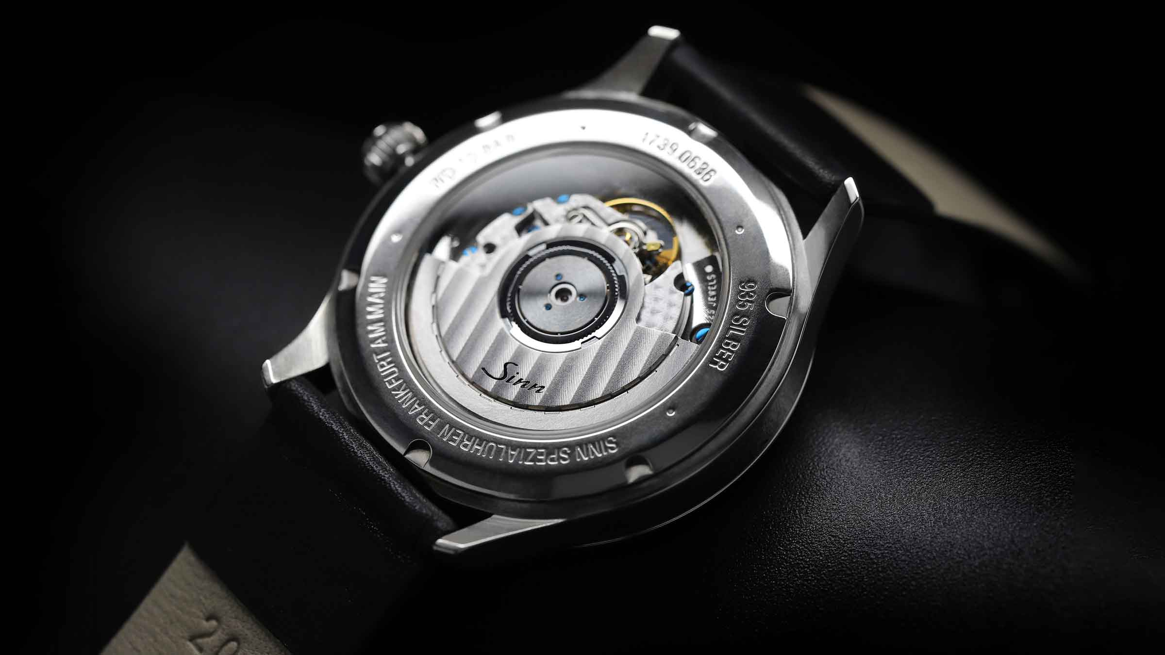 Sinn watch with see-through case back and Argentium case on dark background.