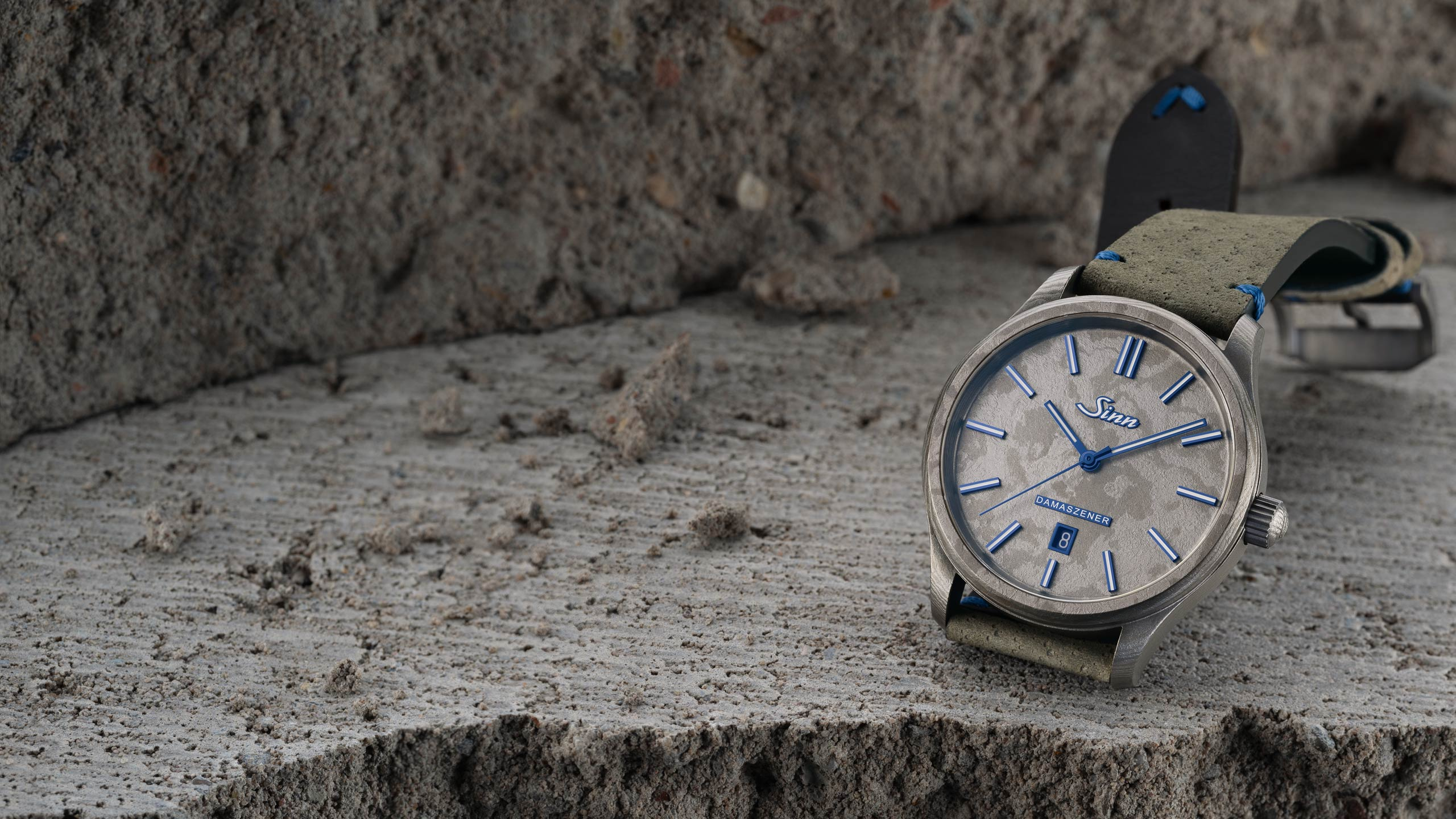 Sinn 1800 TITANDAMASZENER avec bracelet en cuir et détails bleus sur surface pierreuse.