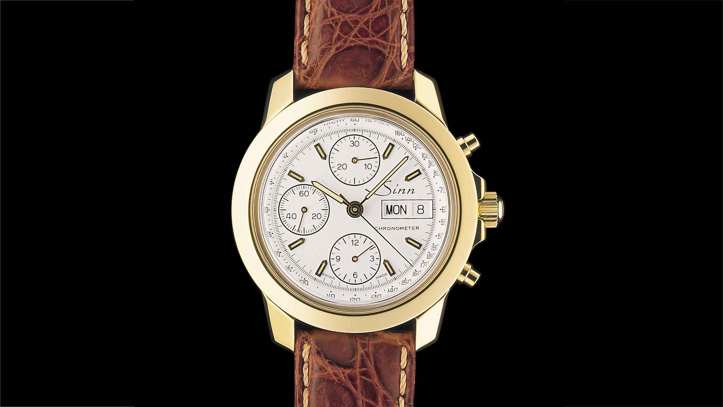 Sinn 2200 Chronometer in gold with white dial, gold indices and brown leather strap on black background.