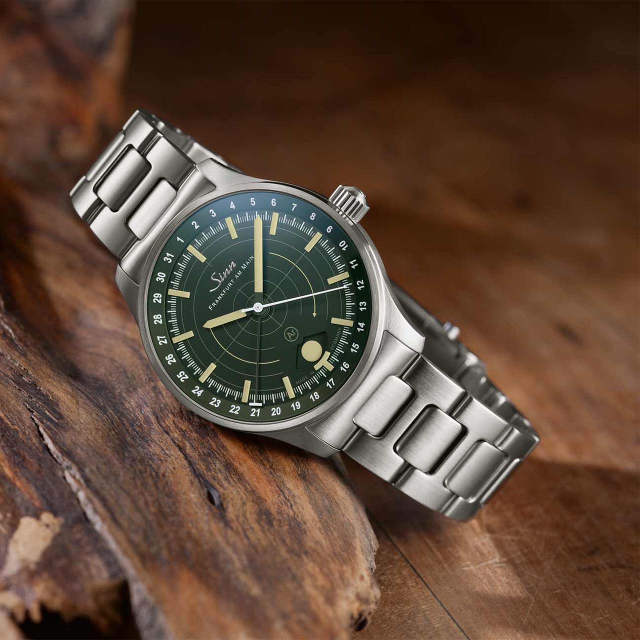 Sinn hunting watch with green dial and bold luminous indices on a stainless steel bracelet, placed on rustic wood.