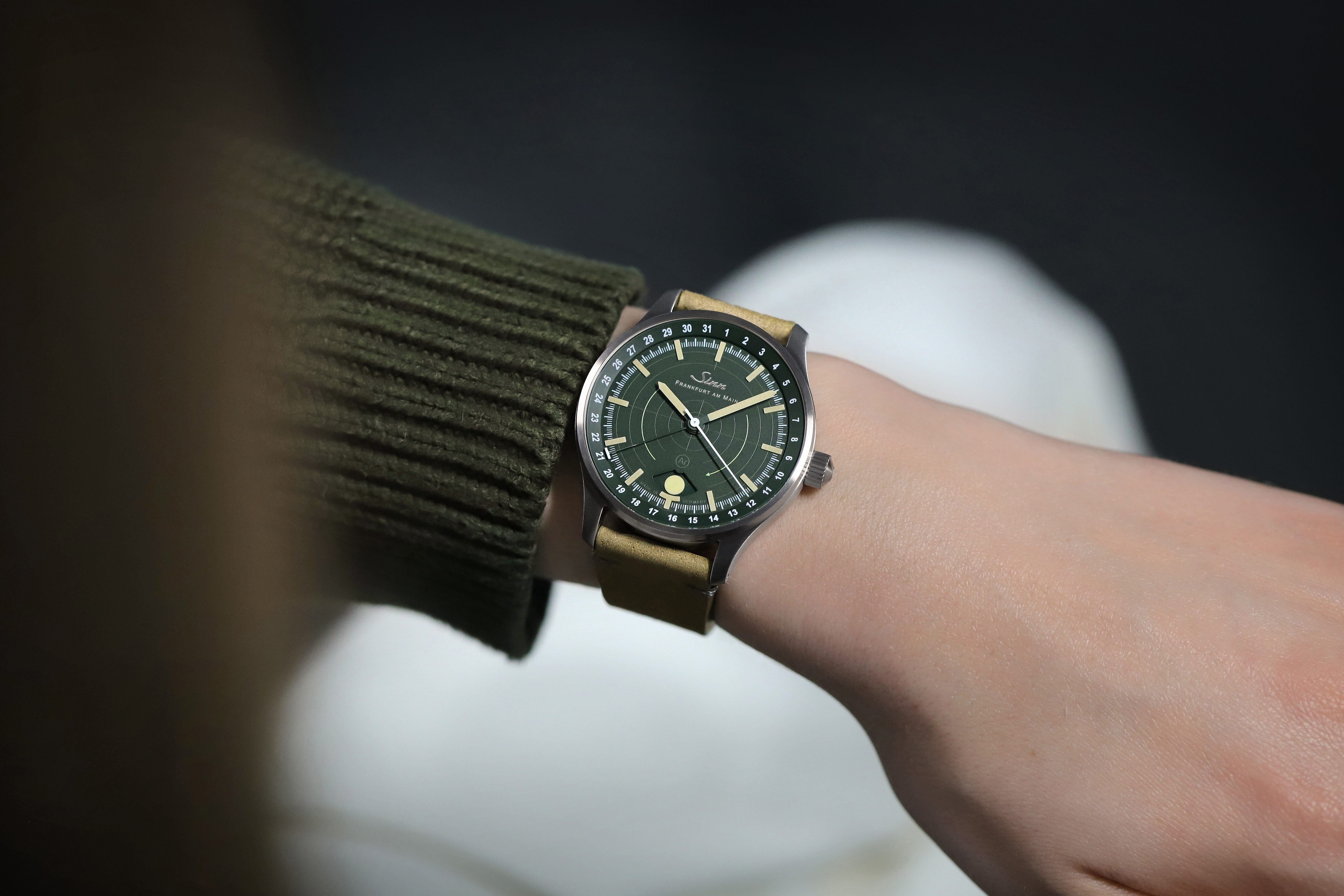 Detailaufnahme einer Armbanduhr mit grünem Zifferblatt und Lederarmband auf dunklem Untergrund.
