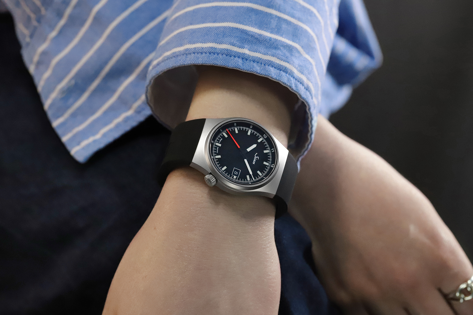 Montre-bracelet avec cadran noir et trotteuse rouge portée au poignet, associée à une chemise rayée.