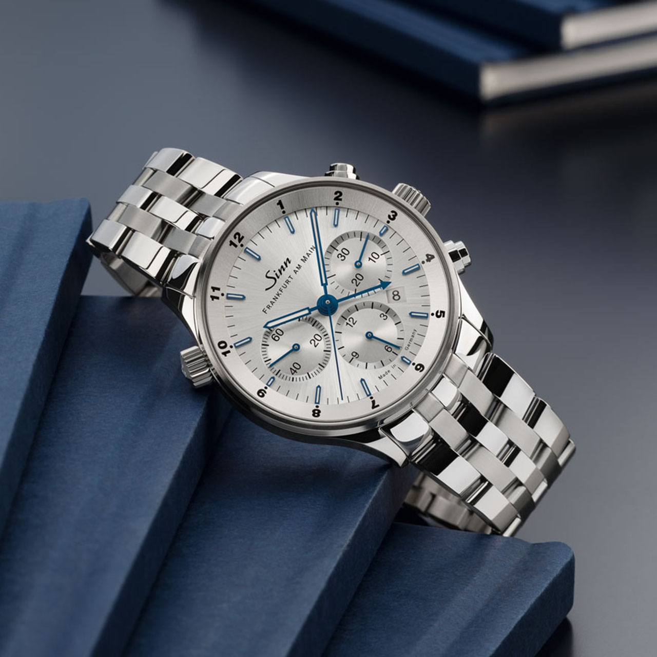 Silver Sinn chronograph with blue-accented hands and subdials on a metal bracelet, displayed on blue blocks.