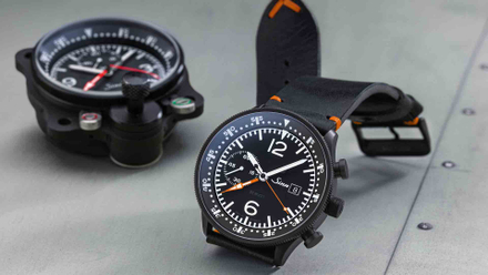 Sinn Fliegerchronograph 717 mit schwarzem Zifferblatt und Lederarmband, inspiriert von historischen Borduhren – im Vordergrund auf einem metallischen Untergrund, daneben ein originales Cockpit-Instrument.