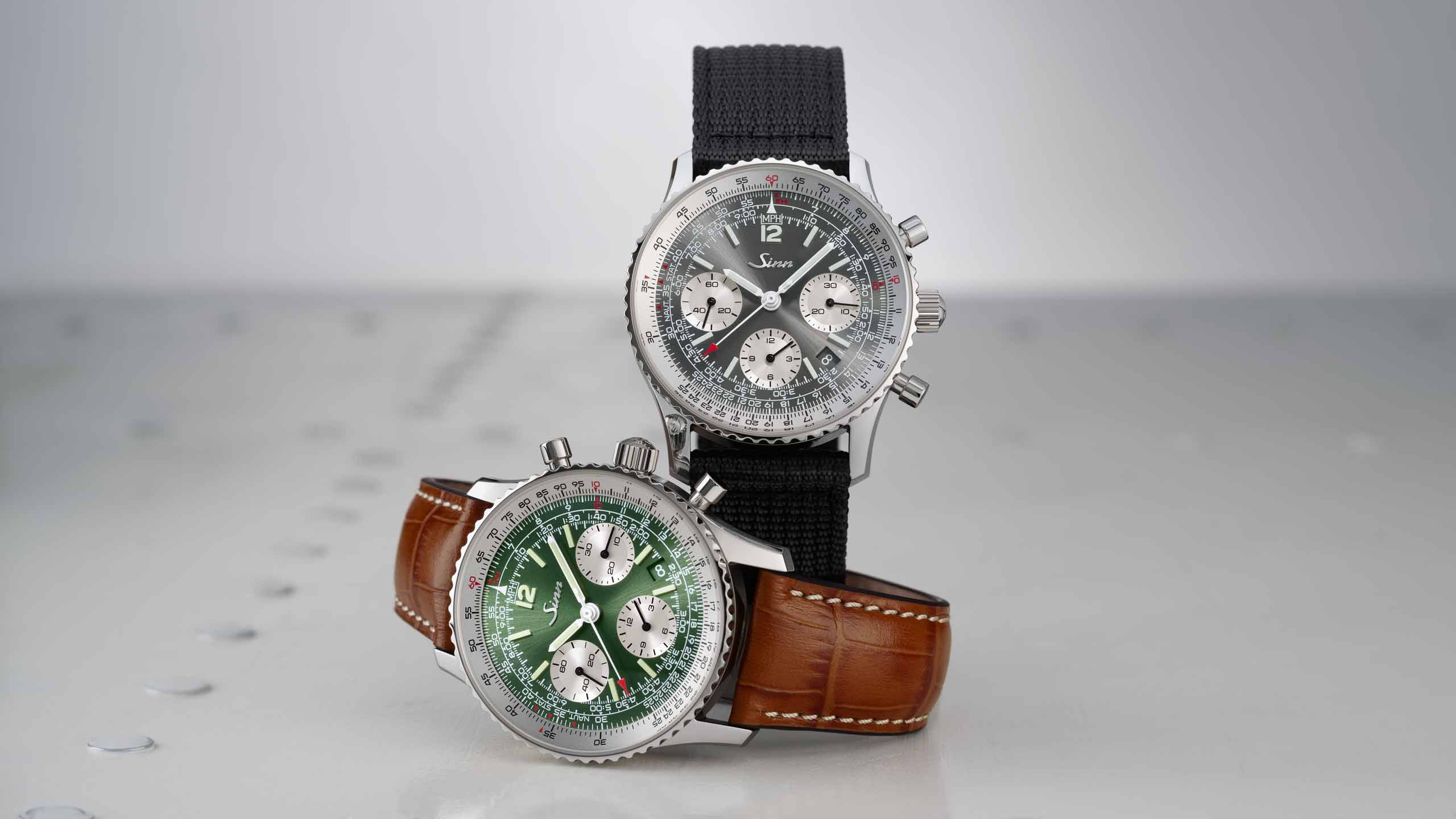                       Two Sinn chronographs, one with a black dial and one with a green dial, shown with textile and leather straps against a light background.
                  