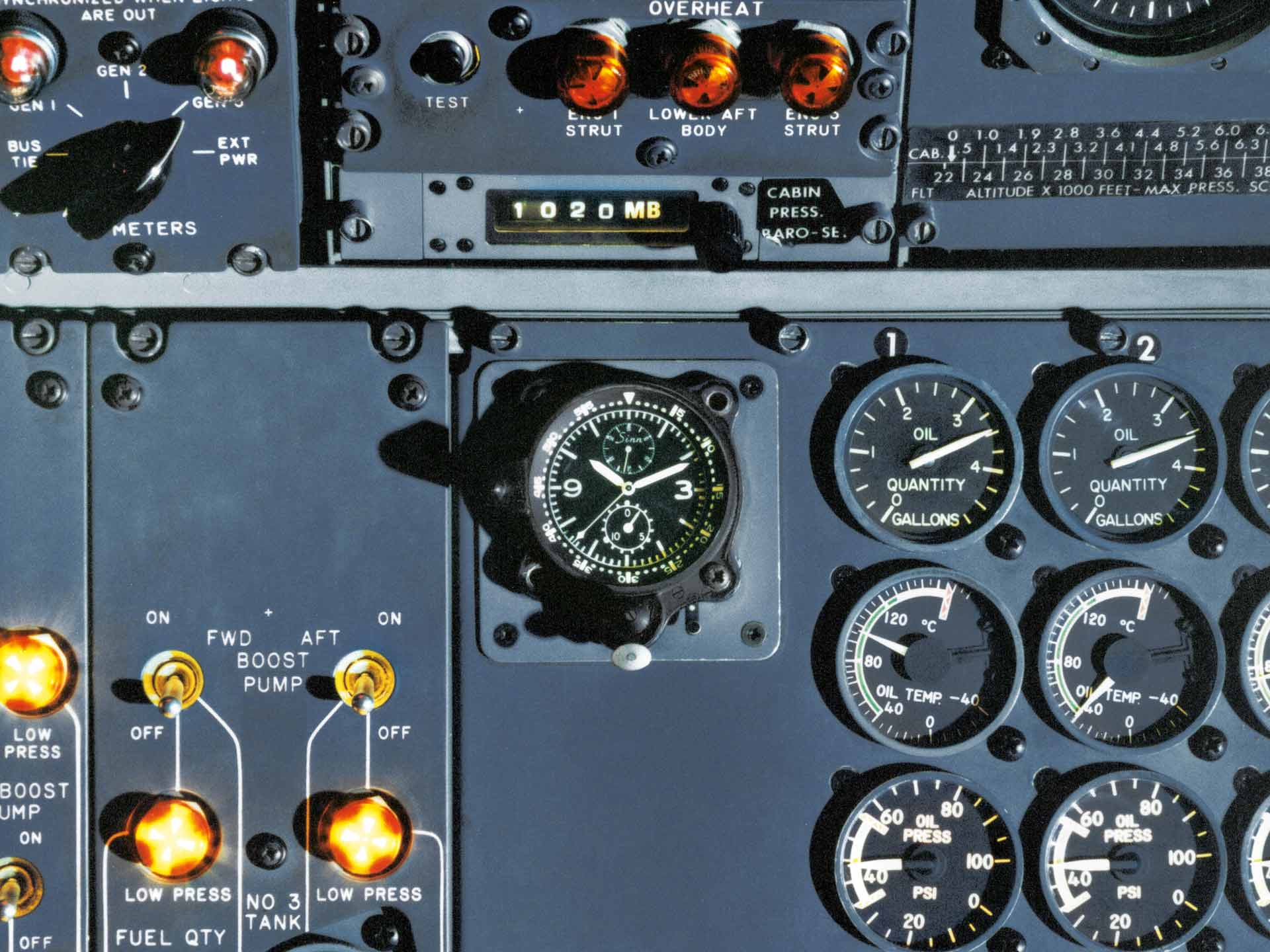 Close-up of a Sinn cockpit clock mounted in an aircraft instrument panel, surrounded by illuminated switches and analog gauges.