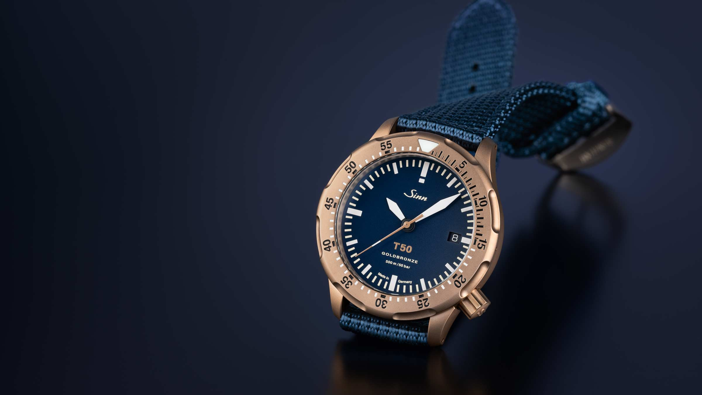 Sinn T50 GOLDBRONZE with textile strap on dark, rough surface.