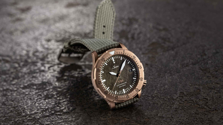 Sinn T50 GOLDBRONZE with gold bronze case and green textile strap, arranged on textured dark surface