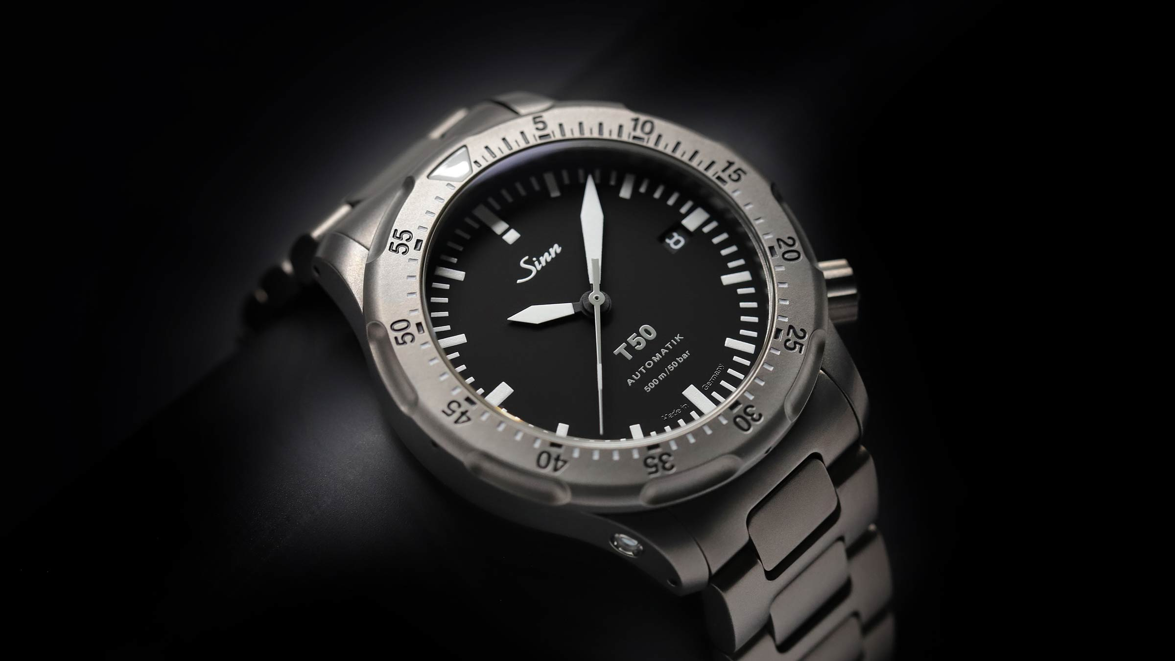 Sinn T50 in titanium with black dial and titanium bracelet on dark background.