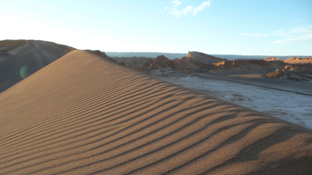                       Sanddüne mit feinen Windrillen im Licht der tiefstehenden Sonne, umgeben von bizarrer Felslandschaft in einer abgelegenen Region Patagoniens
                  