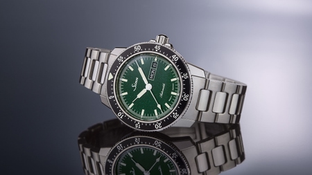                       Sinn 104 St Sa I MG with green dial, luminous hands and stainless-steel bracelet, stylishly arranged on a reflective background with grey gradient.
                  