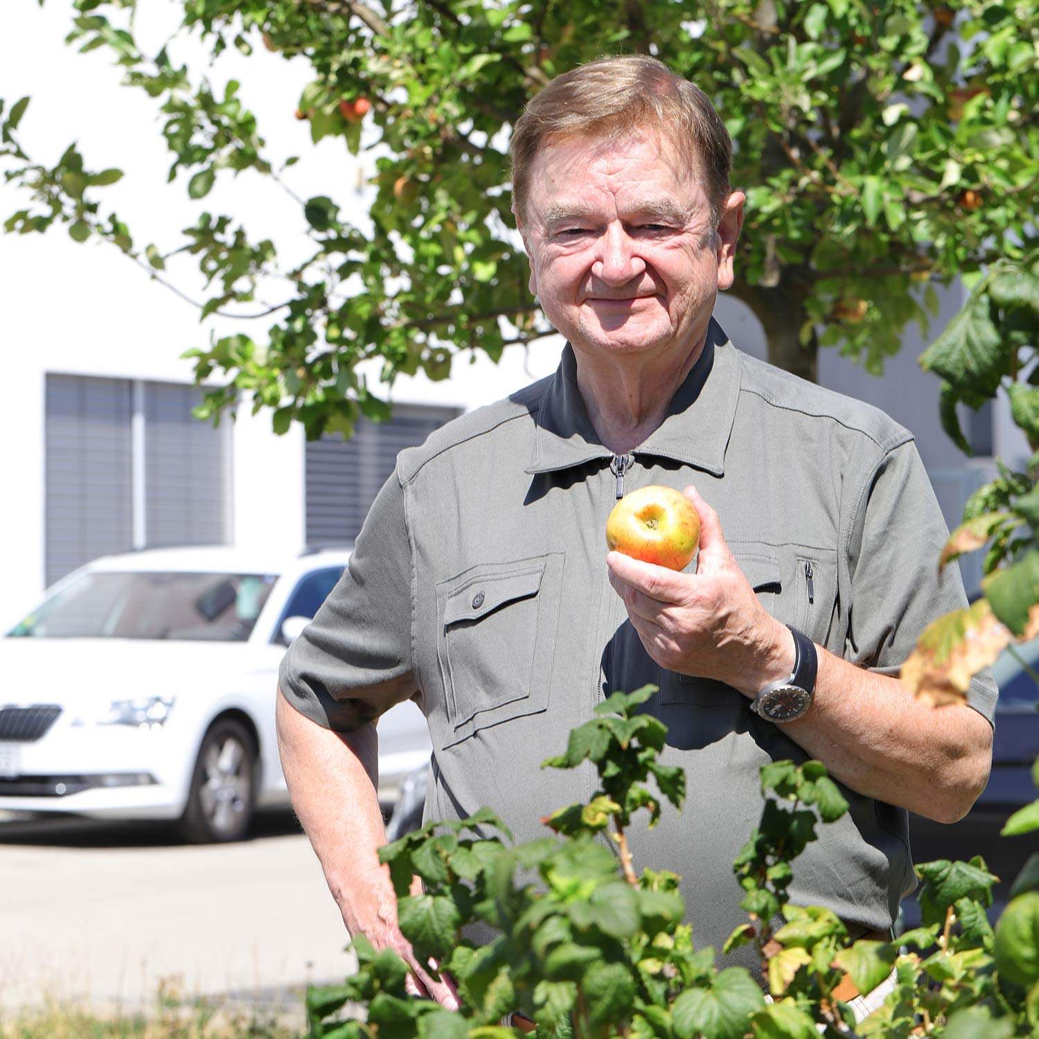 Dipl.-Ing. Lothar Schmidt, owner of Sinn Spezialuhren, stands in front of an apple tree, holding an apple and smiling
