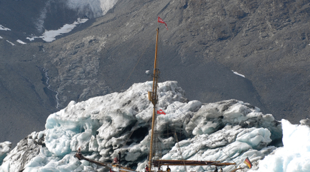 Roter Segelkutter vor Gletschereis in einer eisigen Fjordlandschaft.